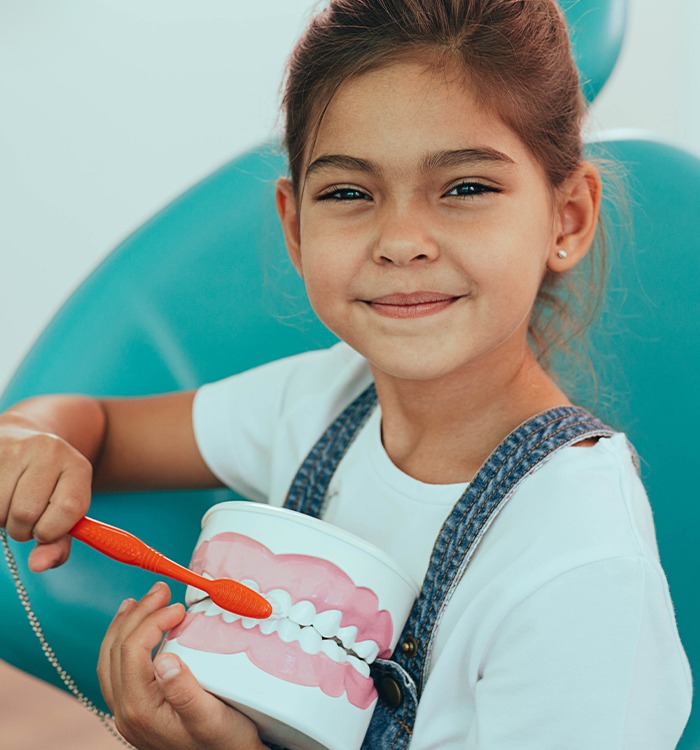 Smiling girl brushing model of teeth