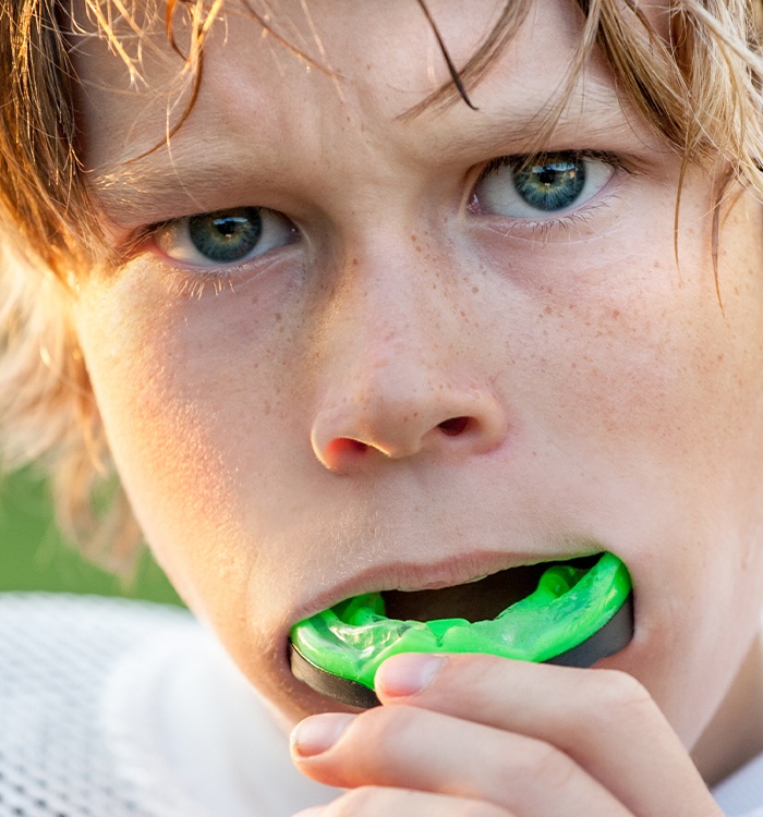 Teen boy placing green athletic mouthguard over his teeth