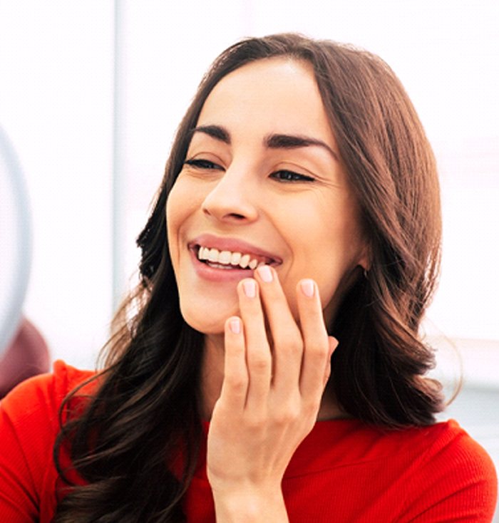 A young woman wearing a red blouse and looking at her new smile in the mirror