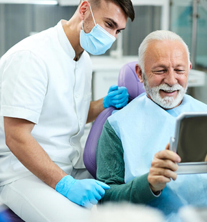 Man in dental chair looking at his smile in mirror