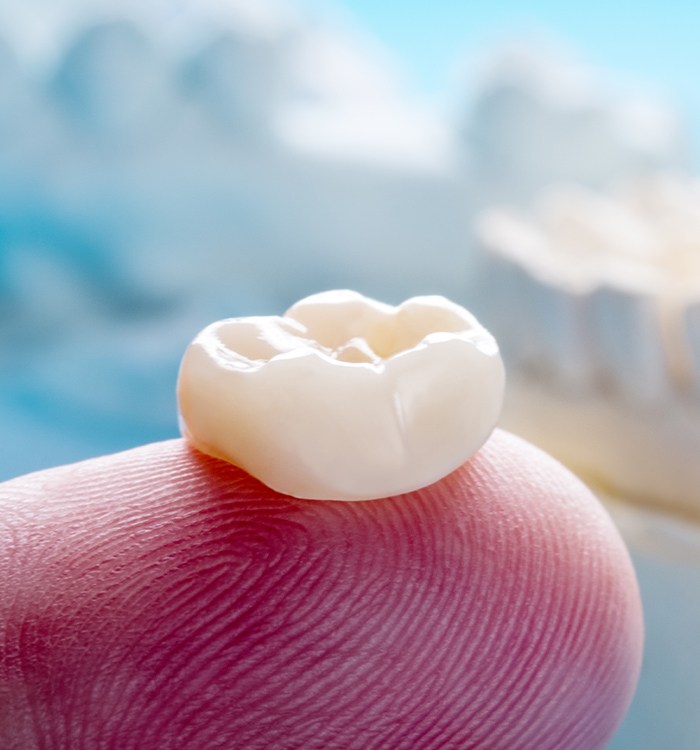 Person holding a dental crown on a fingertip