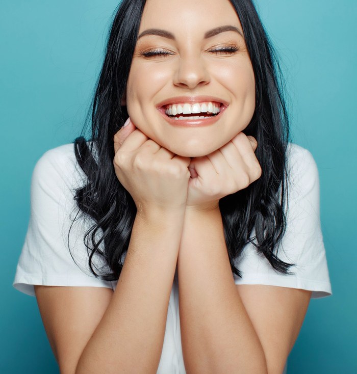 Woman with healthy happy smile pictured against teal background