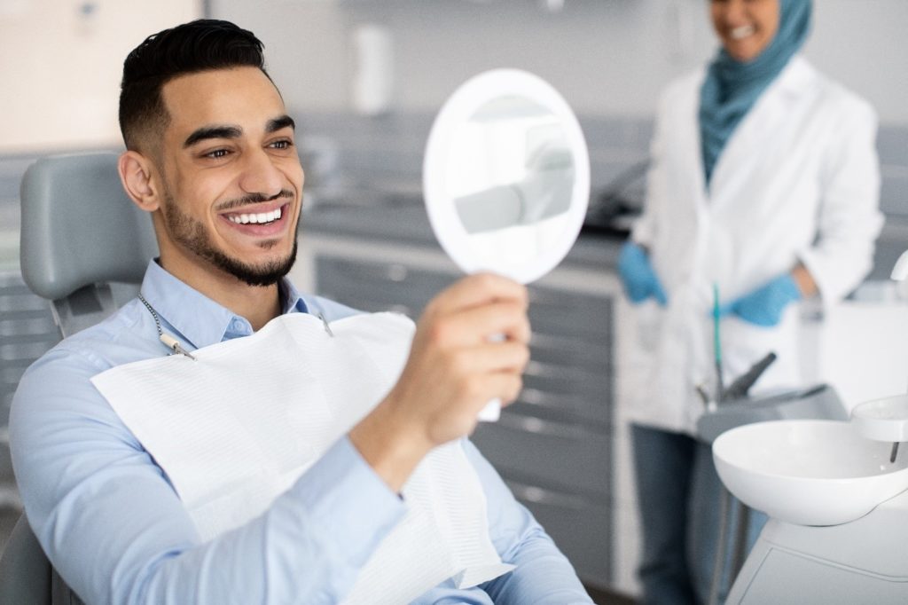 Man with straight teeth smiling at reflection in mirror